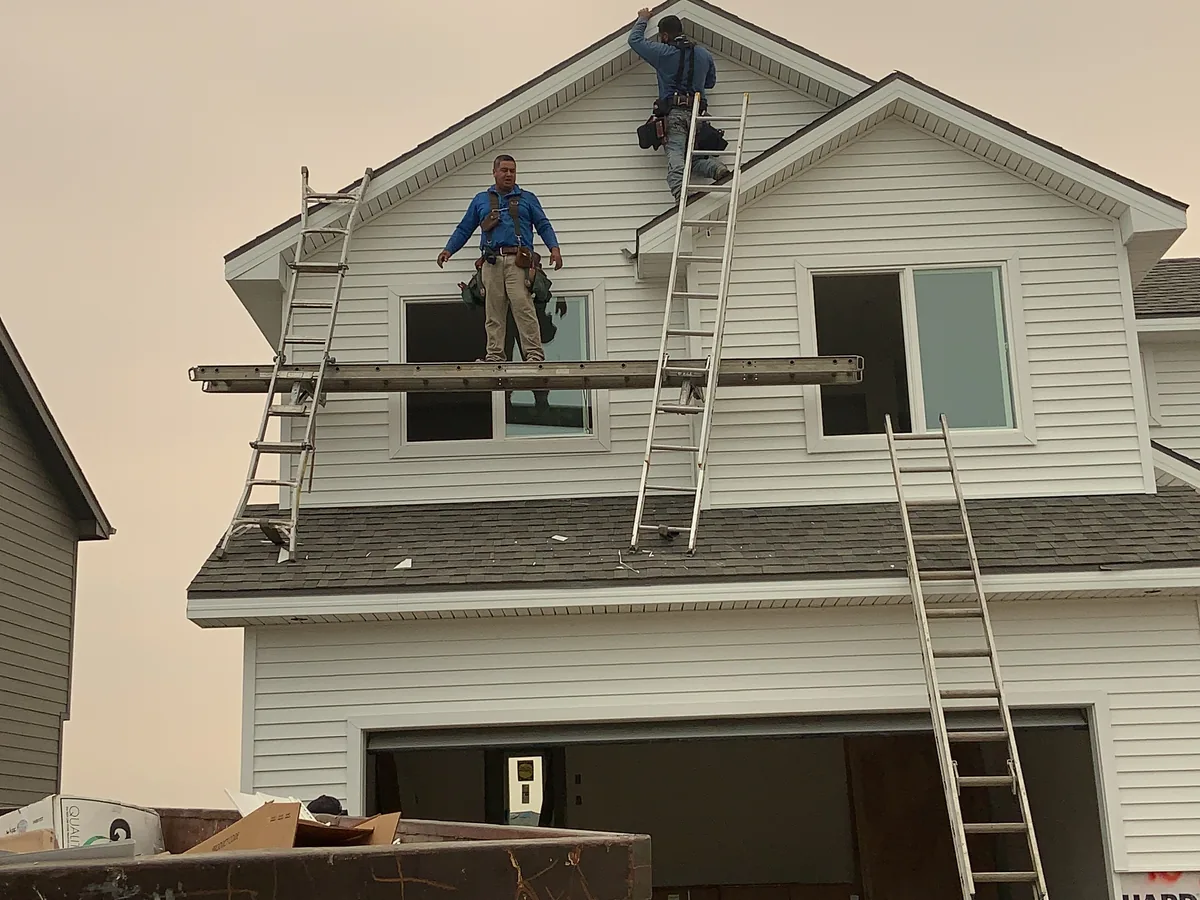Crew installing siding on a two-story home's upper gable